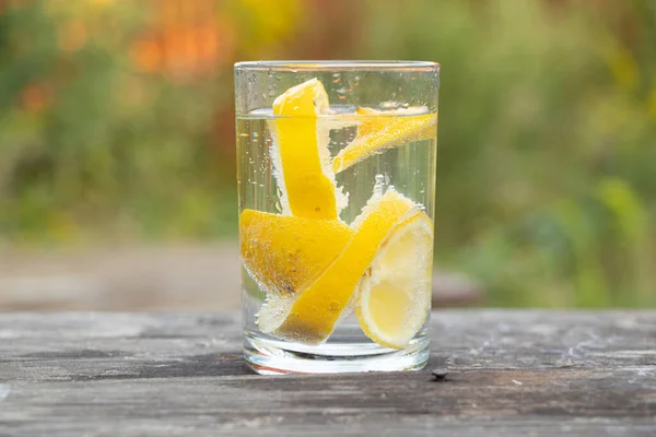 carbonated water with pieces of lemon in a glass on a wooden table outside, lemon juice in a glass, drink, lemonade