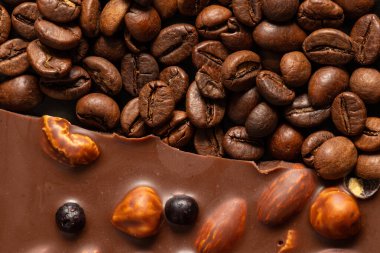 Badem ve fındıklı sütlü çikolata, tüm böğürtlen ve kahve çekirdekleri, kahve ve çikolata arka planda.
