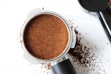 Metal bir kahve filtresi, ölçüm kaşığı ve gevşek kahve telveleri beyaz arka planda yatıyor. Kahve yapma aletleri