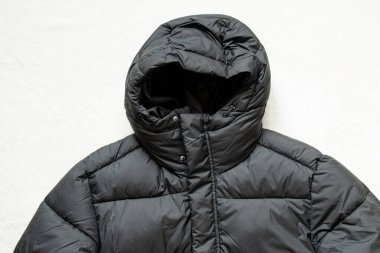 Pliseli, fermuarlı ve kapüşonlu bir erkek kışlık ceketinin siyah örtülü kumaşı. Sıcak dış giysi dokusu