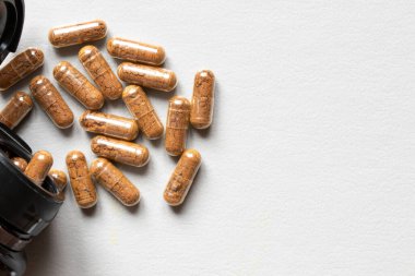 Açık arkaplanda kahverengi toz ve kavanoz bulunan kapsüller, ilaçlar, takviyeler, tedavi ve vitaminlerle ilgili.