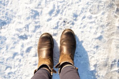Kış yürüyüşü, soğuk koruma, soğuk hava için ayakkabı, kaygan yüzey konuları için karın üzerinde duran kahverengi çizmeli kadın ayakları.