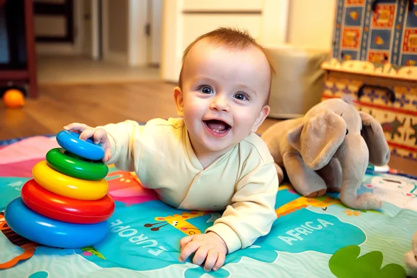 Glimlachende baby liggend op zijn buik en spelen met piramide Stockafbeelding