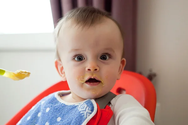 Verrast baby besmeurd met voedsel, eet met zijn mond open Stockfoto