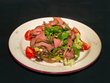 Büyük boy sığır eti, domates ve marul salatası koyu arkaplanda maydanozla süslenmiş.