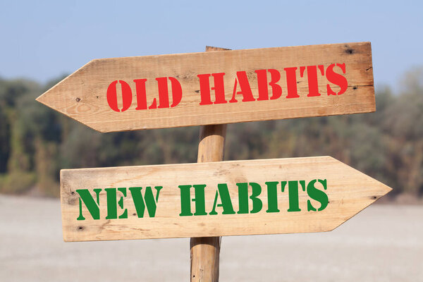 Old Habits versus New Habits text on wooden road sign with left and right arrows.