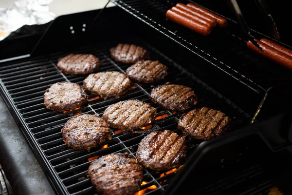 Hamburgers and hot dogs cook on flame charred backyard grill