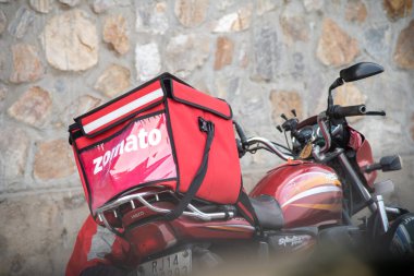 Hindistandaki tek boynuzlu atın binicisine ait büyük kırmızı bir Zomato yiyecek çantasıyla bisiklet.