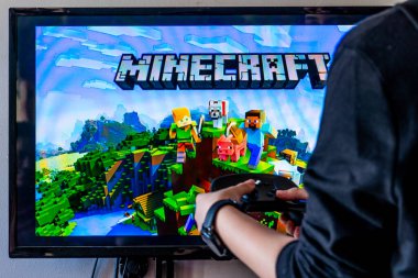 Bir kadın elinde buhar kontrol cihazı tutuyor ve TV ve PC 'de popüler bir video oyunu minecraft oynuyor.