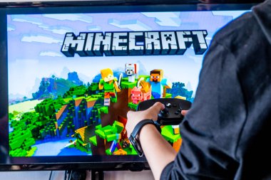Bir kadın elinde buhar kontrol cihazı tutuyor ve TV ve PC 'de popüler bir video oyunu minecraft oynuyor.