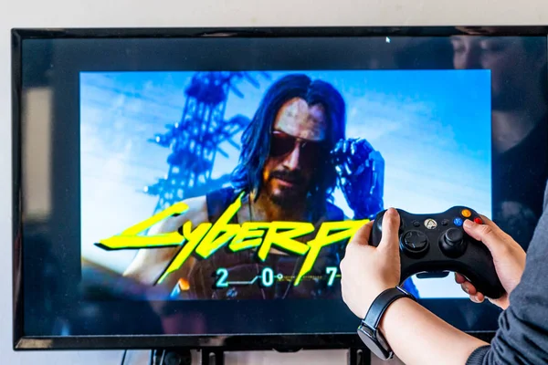 Mulher segurando um controlador xbox e jogando popular jogo de vídeo Cyberpunk 2077 em uma televisão e PC — Fotografia de Stock