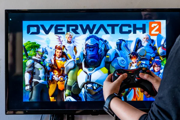 Femme tenant un contrôleur générique et jouant jeu vidéo populaire overwatchon une télévision et un PC — Photo