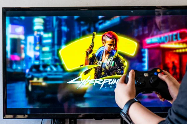 Mujer sosteniendo un controlador xbox y jugando popular videojuego Cyberpunk 2077 en una televisión y PC — Foto de Stock