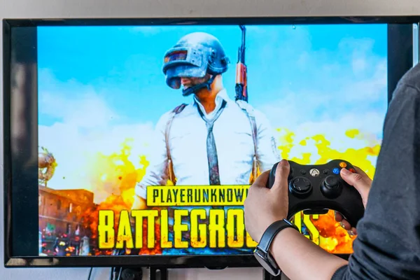 Mujer sosteniendo un controlador xbox y jugando popular videojuego Player Unknowns batalla PUBG en un televisor y PC — Foto de Stock