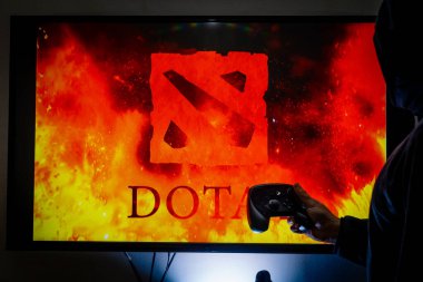 Buhar kontrol cihazı tutan ve popüler DOTA 2 oyununu bir televizyon ve PC 'de oynayan adam.