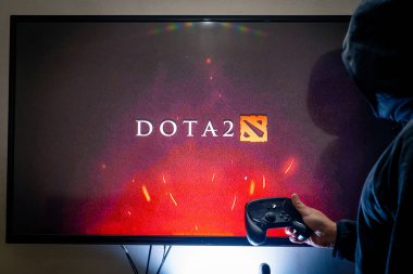 Buhar kontrol cihazı tutan ve popüler DOTA 2 oyununu bir televizyon ve PC 'de oynayan adam.