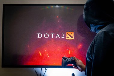 Buhar kontrol cihazı tutan ve popüler DOTA 2 oyununu bir televizyon ve PC 'de oynayan adam.