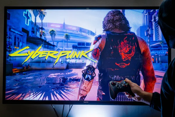 Mulher segurando um controlador de vapor e jogando popular jogo de vídeo Cyberpunk 2077 em uma televisão e PC — Fotografia de Stock