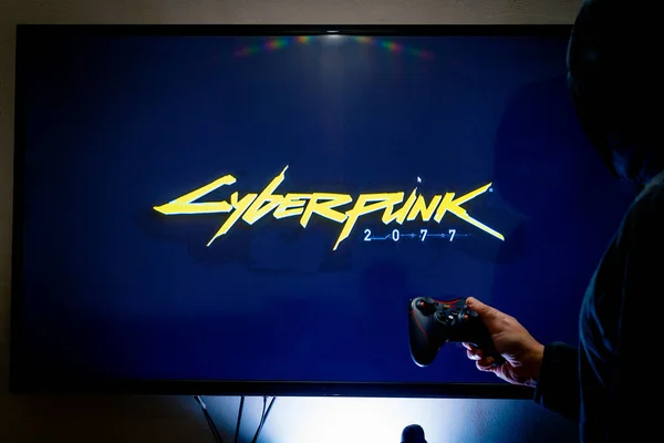 Mulher segurando um controlador de vapor e jogando popular jogo de vídeo Cyberpunk 2077 em uma televisão e PC — Fotografia de Stock
