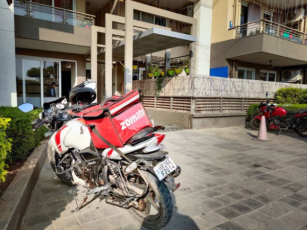 Motociclista con bolsa de zomato rojo entrega de alimentos a un complejo urbano para el unicornio de rápido crecimiento de tecnología de alimentos —  Fotos de Stock