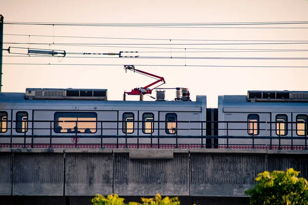 Aerial dusk shots of metro train on elevated bridge with people visible through transparent windows and wires and support visible — Stock Photo, Image