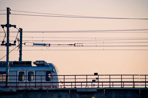 Vue aérienne du crépuscule d'un train de métro sur un pont surélevé avec des personnes visibles à travers des fenêtres et des fils transparents et un soutien visible — Photo