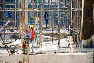 Şafakta Hindistan 'da inşaat alanında işçiler, insanlar, işçiler, mühendisler kadın rengarenk giysiler içinde beton sütunlar arasında çalışan inşaat işçileri.