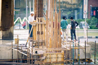 Alacakaranlıkta Hindistan 'da inşaat alanında işçiler, insanlar, işçiler, rengarenk giysiler içindeki mühendisler beton sütunların arasında çalışıyor.