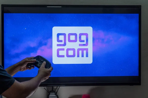 Hombre sosteniendo un controlador frente a la pantalla de carga de la buena tienda de juegos GOG con títulos gratuitos DRM como Cyberpunk witcher y más — Foto de Stock