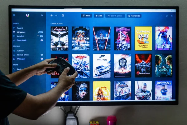 Man holding a steam controller in front of the steam good old games gog epic store library screen choosing a game to play for entertainment leisure addiction — Stock Photo, Image