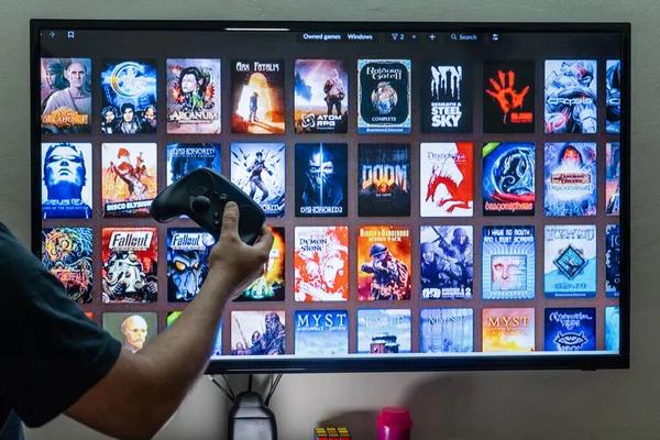 Homem segurando um controlador de vapor na frente do vapor bom velho jogos gog épico loja biblioteca tela escolher um jogo para jogar para entretenimento lazer vício — Fotografia de Stock