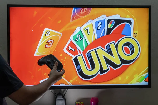 Bir ekranın önünde elinde denetleyici bulunan adam, oyuncuların eğlenmesi için çevrimiçi bir uygulamaya dönüştürülmüş Uno oyununu oynuyor. — Stok fotoğraf