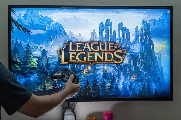 Homem segurando controlador de vapor na frente de uma tela carregando o popular RPG MMORPG liga de lendas um jogo popular muito amado com milhões de jogadores online — Fotografia de Stock