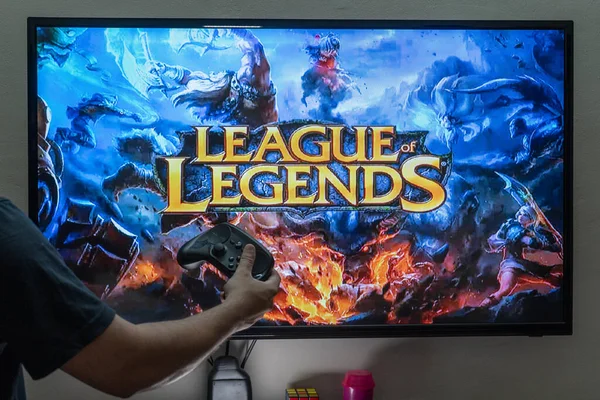 Homem segurando controlador de vapor na frente de uma tela carregando o popular RPG MMORPG liga de lendas um jogo popular muito amado com milhões de jogadores online — Fotografia de Stock