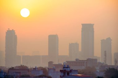 Güneş sisli gökdelenlerin üzerinde yükseliyor. Bangalore hyderabad gurgaon ve diğer Hint şehirlerinde daha küçük evleri olan çok katlı binalar var.