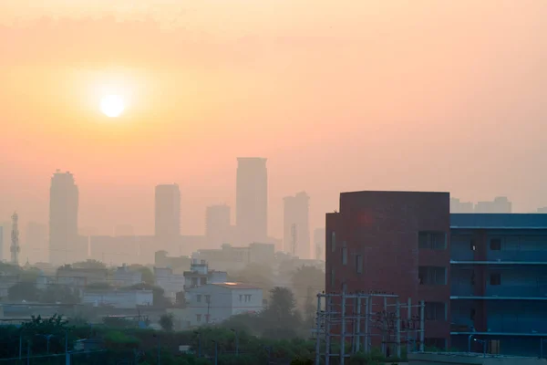 手前にレンガ造りの建物や住宅が建ち並び霧に包まれた高層ビルが立ち昇る太陽との距離を確認 — ストック写真