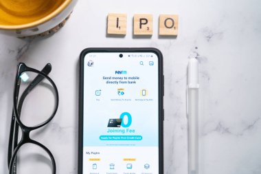 Yakın bir yere yerleştirilmiş kalem ve gözlüklerle cep telefonunda paytm logo ekranı nakitsiz ödemeler için tek boynuzlu at ödeme hizmetleri sağlayıcısının halka açılışını gösteriyor