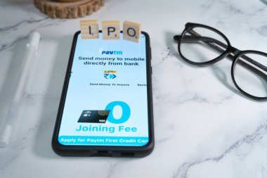Yakın bir yere yerleştirilmiş kalem ve gözlüklerle cep telefonunda paytm logo ekranı nakitsiz ödemeler için tek boynuzlu at ödeme hizmetleri sağlayıcısının halka açılışını gösteriyor