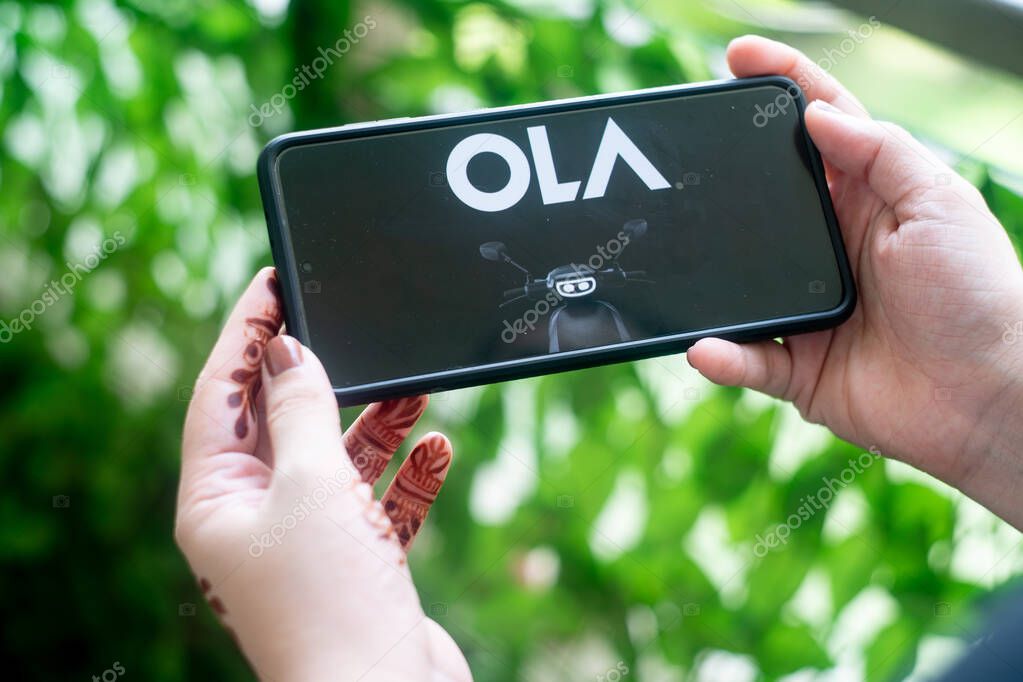 Bangalore, India - circa 2021: Mobile phone smartphone showing website app bor booking Ola Electric new S1 electric vehicle scooter in India asia. With a young woman holding the phone outdoors against