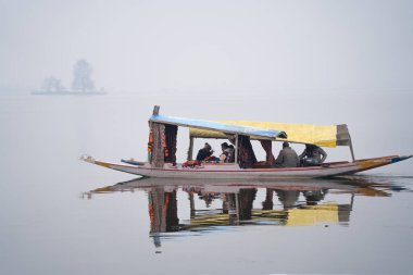 Srinagar, Kashmir, Hindistan - 2 Ocak 2025: Turistler, kışın ortasında kayıkçıların arkasında oturduğu ve donmuş gölün üzerinden geçmek için el kürekleri kullandıkları ünlü dal gölünde kayıkla gezintiye çıkıyorlar.