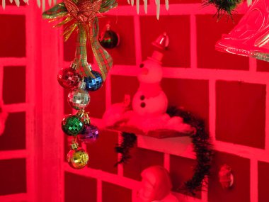 Kırmızı ışıklandırmalı bir odada Noel temalı dekorasyonlar ön planda bir kardan adam ve süsleri gösteriyor.