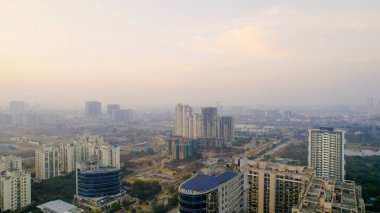 Gurgaon, Delhi, Hindistan - 1 Şubat 2026: Çatı katı güneş panelleri olan Gurgaon konut ve ticari binalarının insansız hava aracı görüntüsü, kentsel gelişimi, yenilenebilir enerji kullanımı ve bulanık şehir manzarası.
