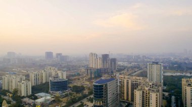 Gurgaon, Delhi, Hindistan - 1 Şubat 2026: Çatı katı güneş panelleri olan Gurgaon konut ve ticari binalarının insansız hava aracı görüntüsü, kentsel gelişimi, yenilenebilir enerji kullanımı ve bulanık şehir manzarası.