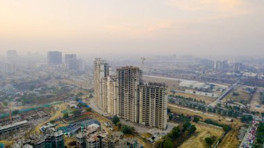 İHA ile inşa halindeki konut binalarının görüntüsü bulanık siluetli vinç ile Gurgaon 'da kentsel büyüme, gayrimenkul gelişimi ve hava kirliliği vurgulanıyor.