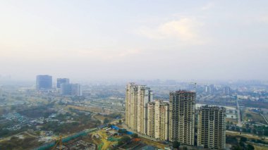 İHA ile inşa halindeki konut binalarının görüntüsü bulanık siluetli vinç ile Gurgaon 'da kentsel büyüme, gayrimenkul gelişimi ve hava kirliliği vurgulanıyor.