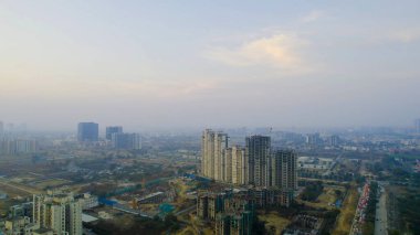 İHA ile inşa halindeki konut binalarının görüntüsü bulanık siluetli vinç ile Gurgaon 'da kentsel büyüme, gayrimenkul gelişimi ve hava kirliliği vurgulanıyor.