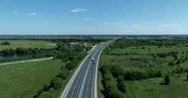 Güneşli bir yaz gününde nehir kıyısındaki köprüye giden yolda arabaların hareketlerinin havadan görüntüsü.