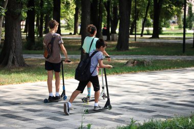 Gençler şehir parkında scooter kullanıyor.
