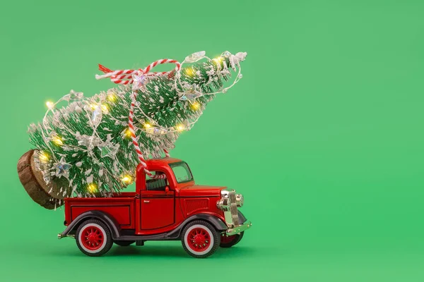 Kırmızı küçük oyuncak kamyonet yeşil arka planda parlayan Noel ağacı ışıklarıyla.
