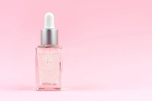 Camdan şeffaf bir maket şişesi. Düşürücü, kozmetik serumu, yağ, pastel pembe arka plan..